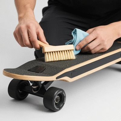 Close-up of a person cleaning the deck and wheels of an electric skateboard with a brush and cloth, focusing on detail